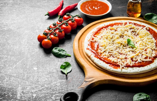 Zubereitung Pizza: Ausgerollter Teig mit Tomatenmark, Käse und Kirschtomaten