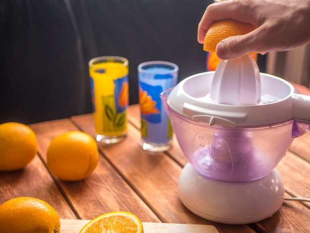 Zubereitung von frischem Orangensaft Smoothie mit Saftpresse auf einer Holzoberfläche