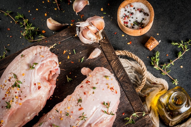 Zubereitung von Speisen Mittagessen Fleisch Hähnchenfilet mit Haut roh Auf einem Schneidebrett mit Gewürzen Thymian Knoblauch Olivenöl Salz Pfeffer Holzbrett schwarzen Stein Hintergrund