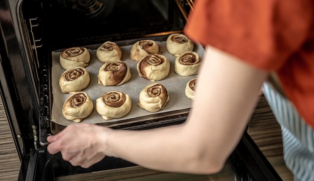 Zubereitung von Zimtschnecken. Eine Frau legt Brötchen auf ein Backblech.