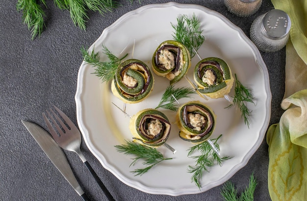 Foto zucchini e rolos de berinjela com alho e queijo creme em um prato em fundo cinza vista superior