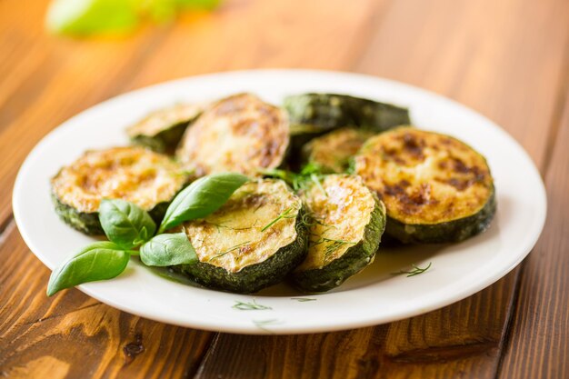 Zucchini in Kreisen mit Gewürzen und Kräutern in einem Teller auf einem Holztisch gebraten