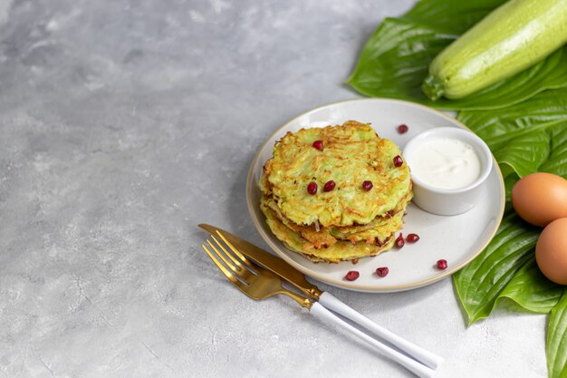 Zucchini-Krapfen, vegetarische Zucchini-Krapfen, serviert mit frischen Kräutern und saurer Sahne.