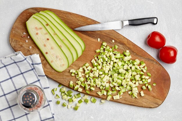 Zucchini-Zucchini-Würfel in Scheiben geschnitten auf einem Holzschneidebrett Tomaten-Knoblauch auf einem Beton-Leuchttisch