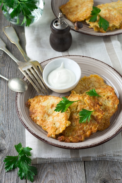 Zucchinikrapfen, hausgemachte vegetarische Zucchinipfannkuchen mit frischen Kräutern und Joghurtsauce auf einem weißen Keramikteller auf altem Holztisch. Rustikaler Stil. Selektiver Fokus. Draufsicht. Platz für Text.