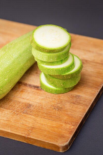 Zucchinischeiben auf Holzschneidebrett. Frische grüne Zucchini ganz und auf dem Schneidebrett in Scheiben schneiden