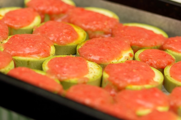 Zucchinischeiben mit Gewürzen und Tomatensauce auf Pergamentpapier Vegetarisches Essen Closeup