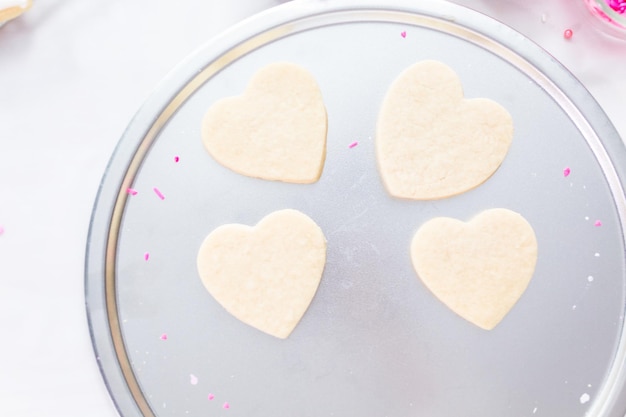 Zuckerkekse in Herzform mit königlichem Zuckerguss und rosa Streuseln zum Valentinstag dekorieren.