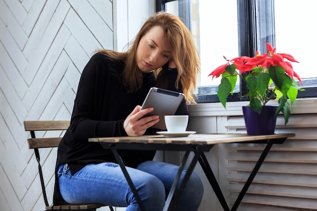 Zufällige Frau, die Kaffee trinkt und mit Tablet-PC arbeitet.