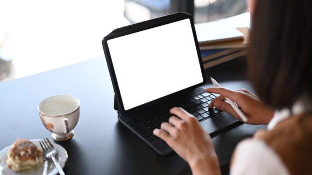 Zufällige junge Frau mit dem Stift, der auf digitalem Tablett am Café arbeitet.