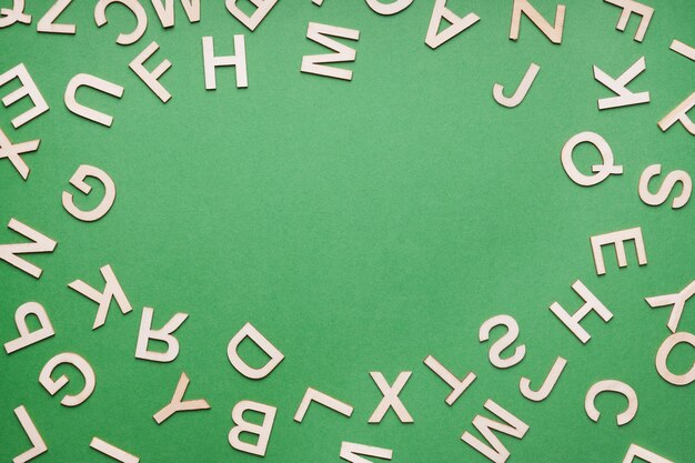 Zufälliger Holzbuchstabenrahmen auf grünem Papierhintergrund