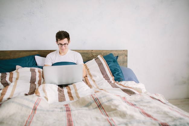 Zufälliger junger Mann, der Laptop im Bett zu Hause benutzt