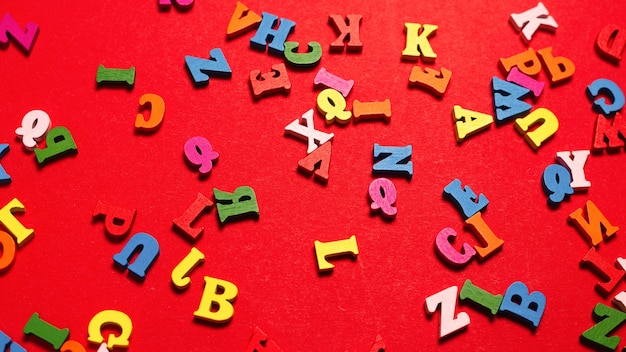 Zufälliges buntes Alphabet auf rotem Grund, bunte Buchstaben. Ansicht von oben.