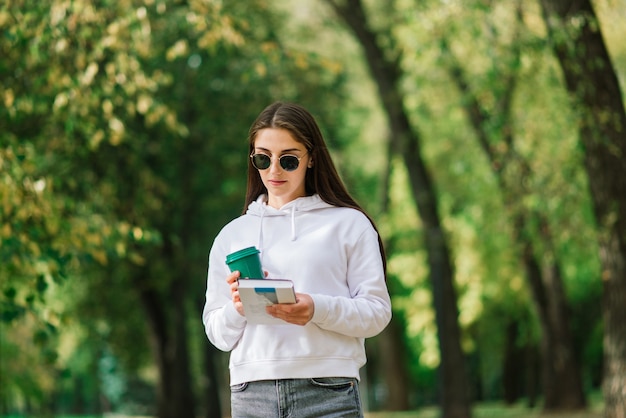 Zufriedene erwachsene Frau, die im Sommer eine Kaffeetasse im Park hält