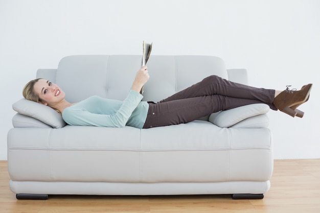 Foto zufriedene frau des inhalts, welche die zeitung liegt auf couch hält