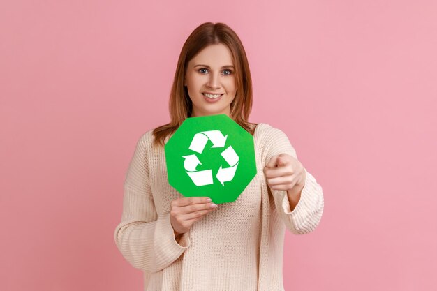 Zufriedene junge erwachsene Frau mit grünem Recycling-Schild zum Schutz der Umwelt, die auf die Kamera zeigt