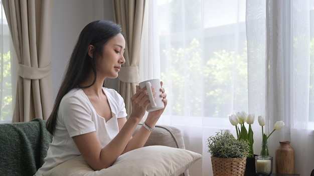 Zufriedene junge Frau, die sich auf der Couch entspannt und morgens heißen Kaffee trinkt