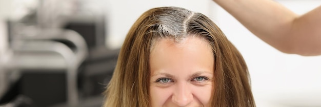 Foto zufriedene kundin sitzt beim friseurmeister und trägt mit einer bürstenausrüstung färbemittel auf das haar auf