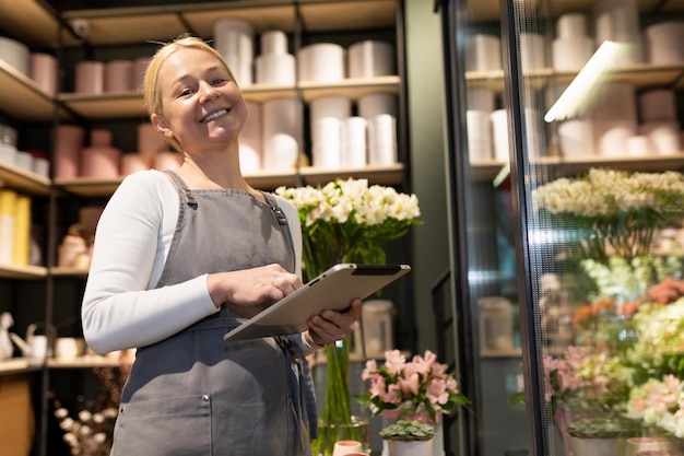 Zufriedene selbstständige Besitzerin eines Blumenladens mit einem Tablet in ihren Händen neben a