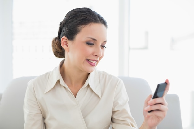 Zufriedene stilvolle Brunettegeschäftsfrau, die ihren Handy betrachtet