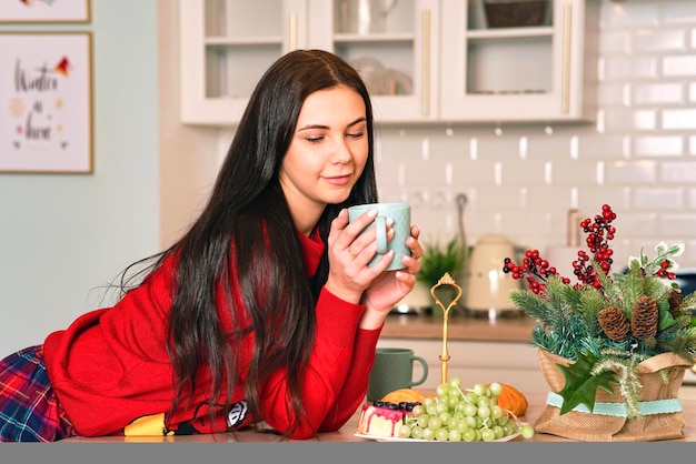 Zufriedene süße Frau, die zu Hause Kaffee in ihrer Küche trinkt, süße Frau, die eine Tasse guten Morgen hält