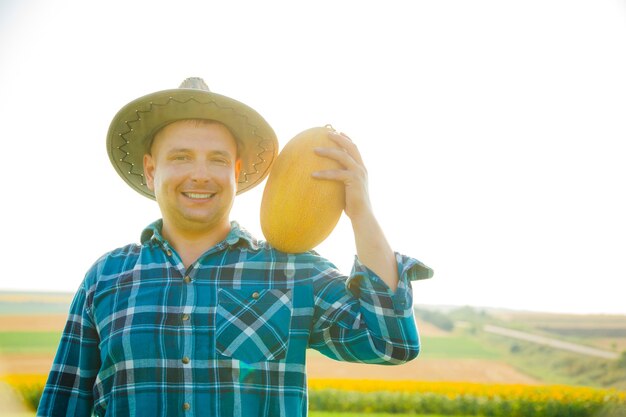 Zufriedener Bauer hat eine Melone auf der Schulter der Mann mit dem Hut schaut in die Kamera und hält ...