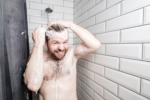 Zufriedener Mann, der in der Dusche unter einem Wasserstrahl mit Schaum eingeseift wurde