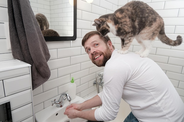 Zufriedener Mann wäscht seine Hände unter einem Wasserstrahl und seiner entzückenden Katze