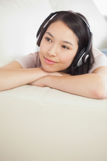 Zufriedenes asiatisches Mädchen, das auf dem Sofa liegt und Musik hört