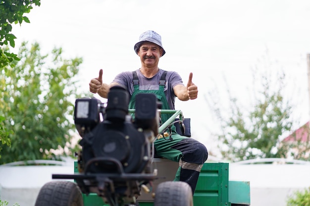 Zufriedenes Bauernporträt, das hinter dem Rad eines zweirädrigen Traktors sitzt