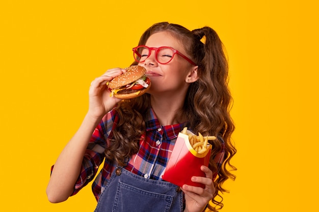 Foto zufriedenes junges mädchen mit frischem burger und pommes frites, das fast food genießt