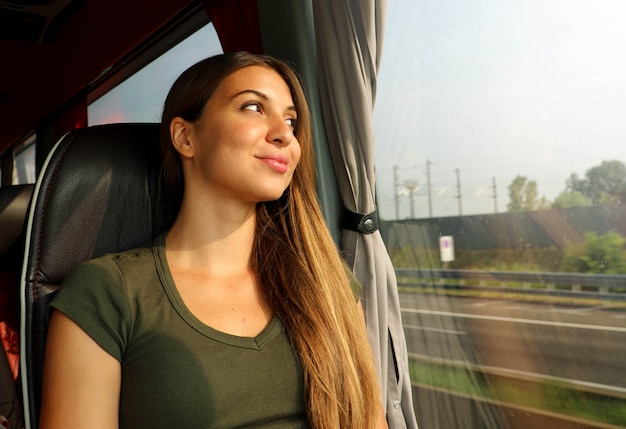 Zug- oder Busreisender. Schöne lächelnde Frau, die durch das Fenster während der Reise auf öffentlichen Verkehrsmitteln schaut.