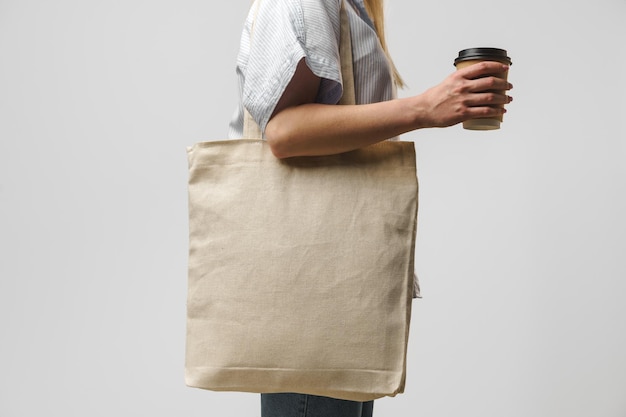 Zugeschnittene Frau mit Baumwolltasche und Kaffeetasse aus Papier Studioaufnahme