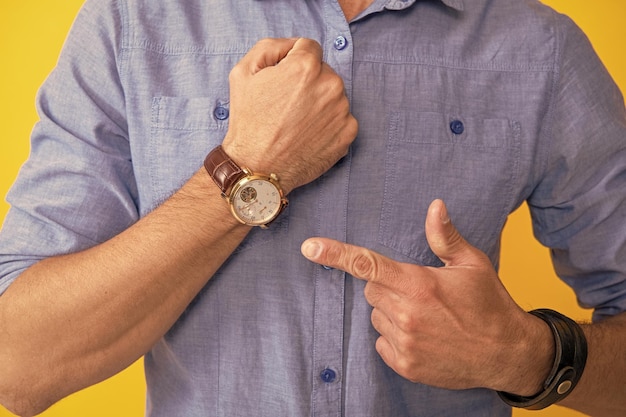 Zugeschnittener Mann, der mit dem Finger auf die Uhr auf gelbem Hintergrund zeigt Zeit
