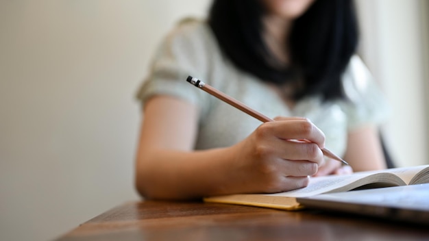 Zugeschnittenes Bild Eine junge asiatische College-Studentin, die Hausaufgaben macht und auf einem Notebook schreibt