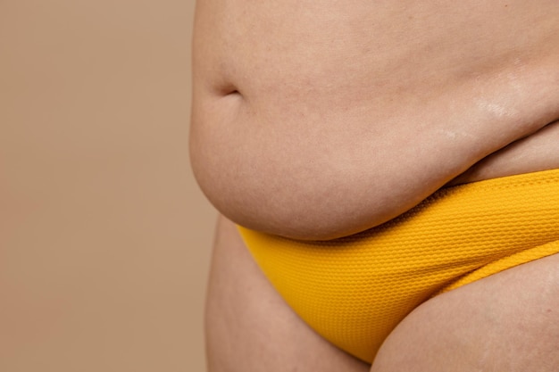 Zugeschnittenes Bild von übergewichtiger, fetter, schwangerer Frau, schlaffer Bauch mit Fettleibigkeit, überschüssigem Fett in gelben Hosen. Schneller Gewichtsverlust