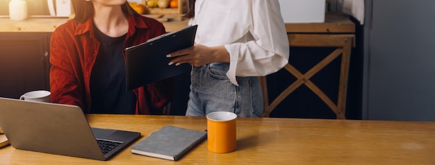Zugeschnittenes Foto einer asiatischen Freiberuflerin, die eine Kaffeetasse in der Hand hält und am Arbeitsplatz Planung und Analyse des Finanzberichts, Geschäftsplans, Investitionsfinanzierungsanalyse durchführt