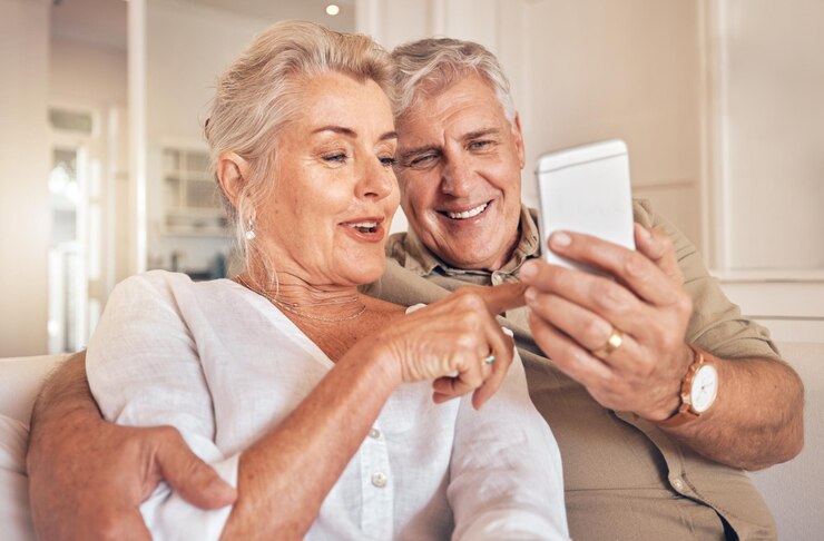 Zuhause lächelnd und älteres Paar mit einem Smartphone, Liebe und schöne Zeit mit Social-Media-Chats und SMS. Alter Mann und ältere Frau auf dem Handy mit mobiler Glücks-App und Entspannung mit Verbindung