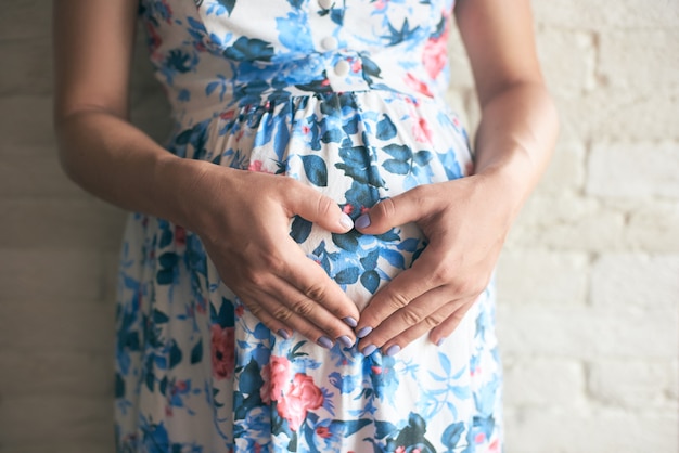 Zukünftige Mutter, die Hände auf Bauch hält und Herz zeigt