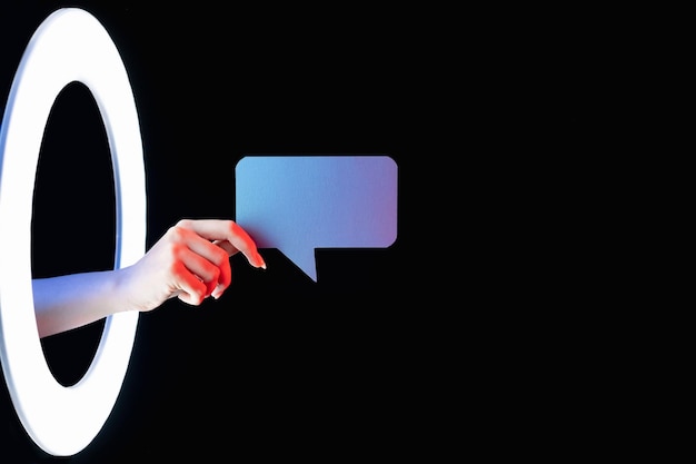 Zukünftige Nachricht Dialogsymbol Futuristische virtuelle Kommunikation Weibliche Hand mit blauer, leerer Chat-Textblase in LED-Lichtring isoliert auf dunkelschwarzem, leerem Raumhintergrund