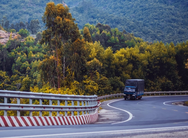 Zukunftskonzept der Zeitumstellung Schönheitspanorama Landschaft Trockene Asphalt-LKW-Wicklungsstraße mit Markierungslinien im bewaldeten Nebelberghintergrund Abendfrühherbst oder Spätsommerlaub