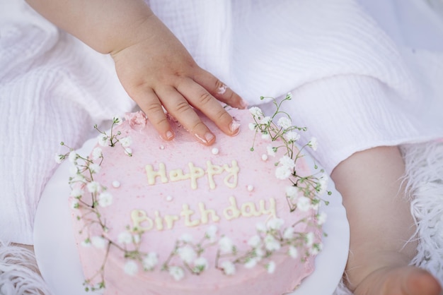 Foto zum ersten geburtstag zerschlagen sie die kuchencreme auf die hände eines kleinen kaukasischen mädchens, das seinen ersten geburtstag feiert