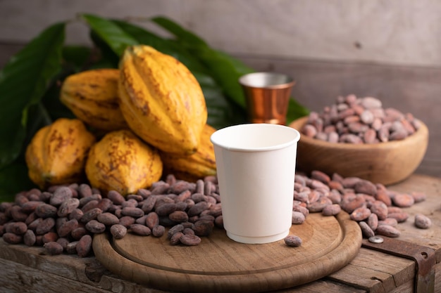 Zum Mitnehmen Heiße Kakaotasse aus weißem Papier auf reifer Kakaoschote und Nibs Kakaobohnen Hintergrund einrichten
