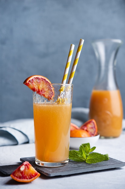 Zumo de naranja dulce con una rodaja de naranja roja y menta sobre un fondo gris