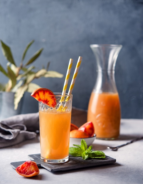 Zumo de naranja dulce con una rodaja de naranja roja y menta sobre un fondo gris