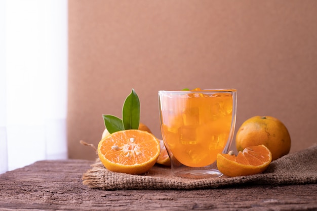 Zumo de naranja frío y naranja en rodajas sobre mesa de madera.