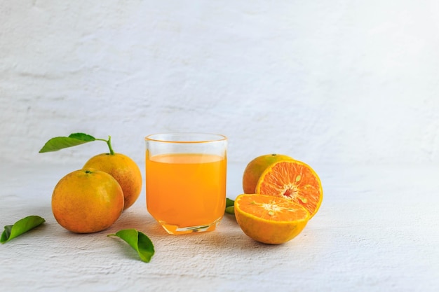 Zumo de naranja recién exprimido en un vaso y cítricos frescos sobre un fondo blanco