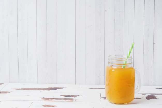 Zumo de naranja en los tarros de cristal y las naranjas frescas en un fondo rústico de madera blanco.