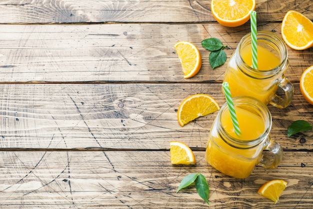 Zumo de naranja en los tarros de cristal y las naranjas frescas en un fondo rústico de madera. Copia espacio