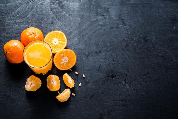 Zumo de naranja en vaso con naranjas crudas sobre fondo negro. copia espacio